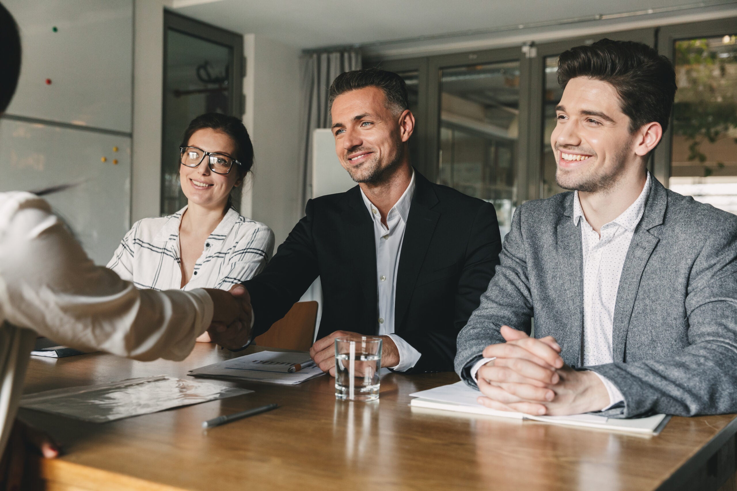 Three business partners in office handshaking with woman, as suc Three business partners in office handshaking with woman, as suc