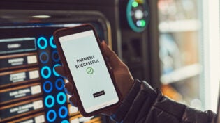 Consumer paying for product at vending machine using contactless method of payment with mobile phone. Woman using payment app on smartphone to buy product. Female hand holding smart phone with payment confirmation on screen