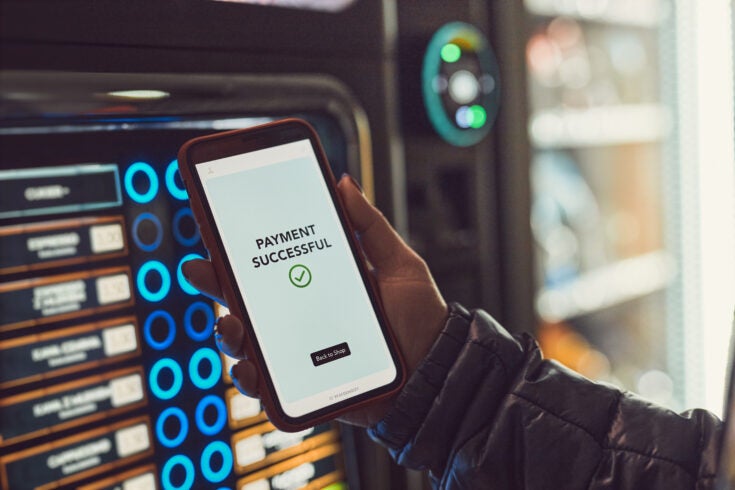 Consumer paying for product at vending machine using contactless method of payment with mobile phone. Woman using payment app on smartphone to buy product. Female hand holding smart phone with payment confirmation on screen
