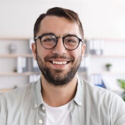Headshot of cheerful mature european man with beard in glasses look at laptop webcam at minimalist living room