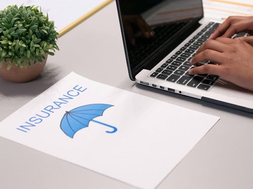 hand typing on laptop next to page marked insurance
