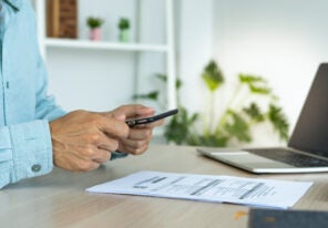 A business man uses his phone to scan a barcode to pay his monthly credit card bill after receiving an invoice. online bill payment concept