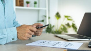 A business man uses his phone to scan a barcode to pay his monthly credit card bill after receiving an invoice. online bill payment concept