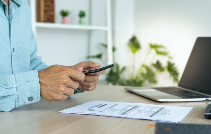 A business man uses his phone to scan a barcode to pay his monthly credit card bill after receiving an invoice. online bill payment concept