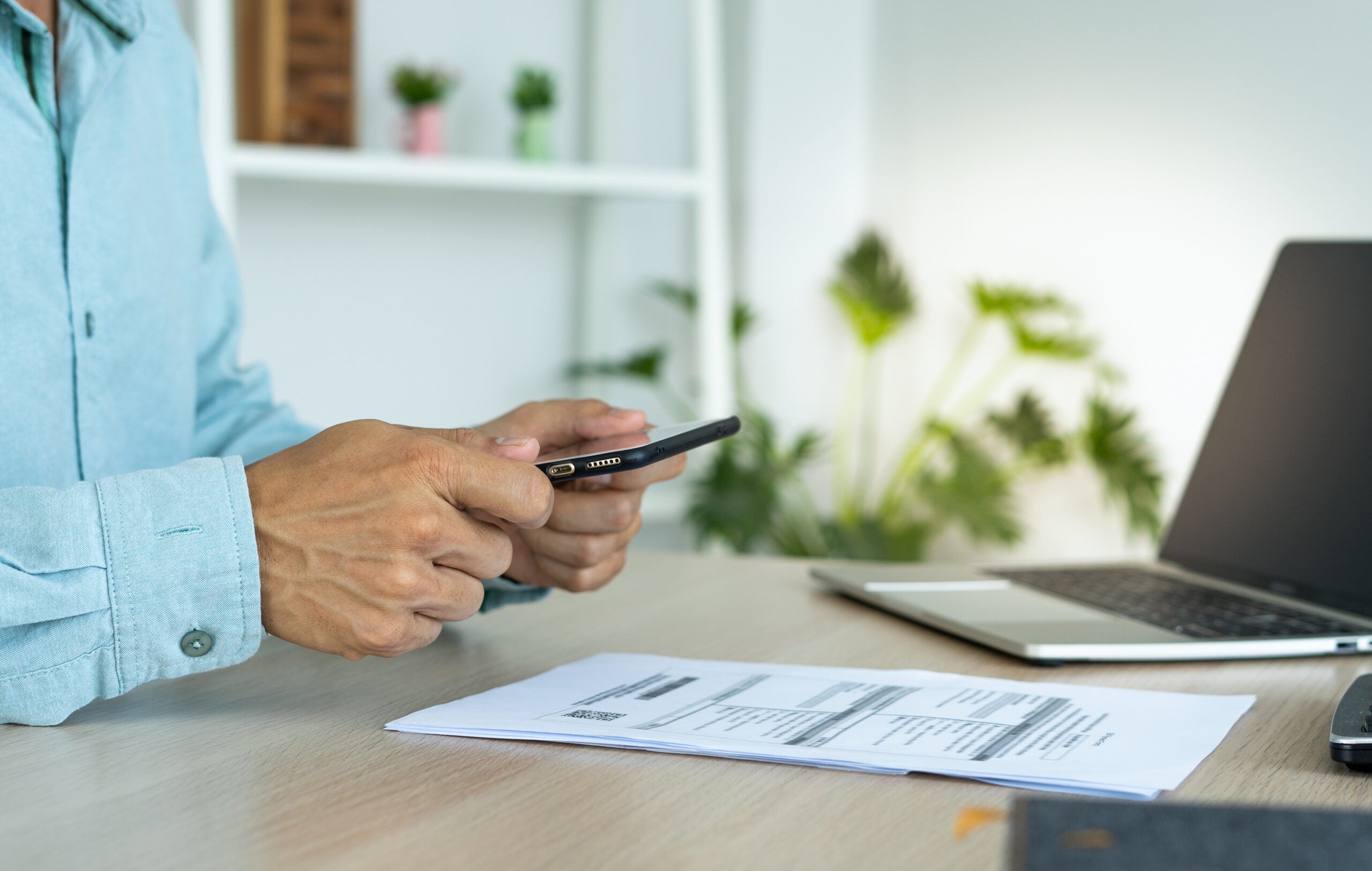 A business man uses his phone to scan a barcode to pay his monthly credit card bill after receiving an invoice. online bill payment concept A business man uses his phone to scan a barcode to pay his monthly credit card bill after receiving an invoice. online bill payment concept
