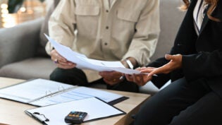 Close up male senior client and female insurance agent sitting on a couch in a house pointing out the agreement condition together, for real estate, business, finance and insurance concept.