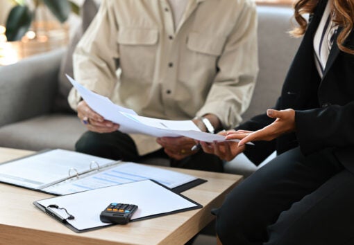 Close up male senior client and female insurance agent sitting on a couch in a house pointing out the agreement condition together, for real estate, business, finance and insurance concept.