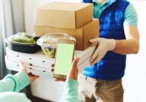 POV of woman using smarthone for ordering online, receiving takeout food from delivery man.