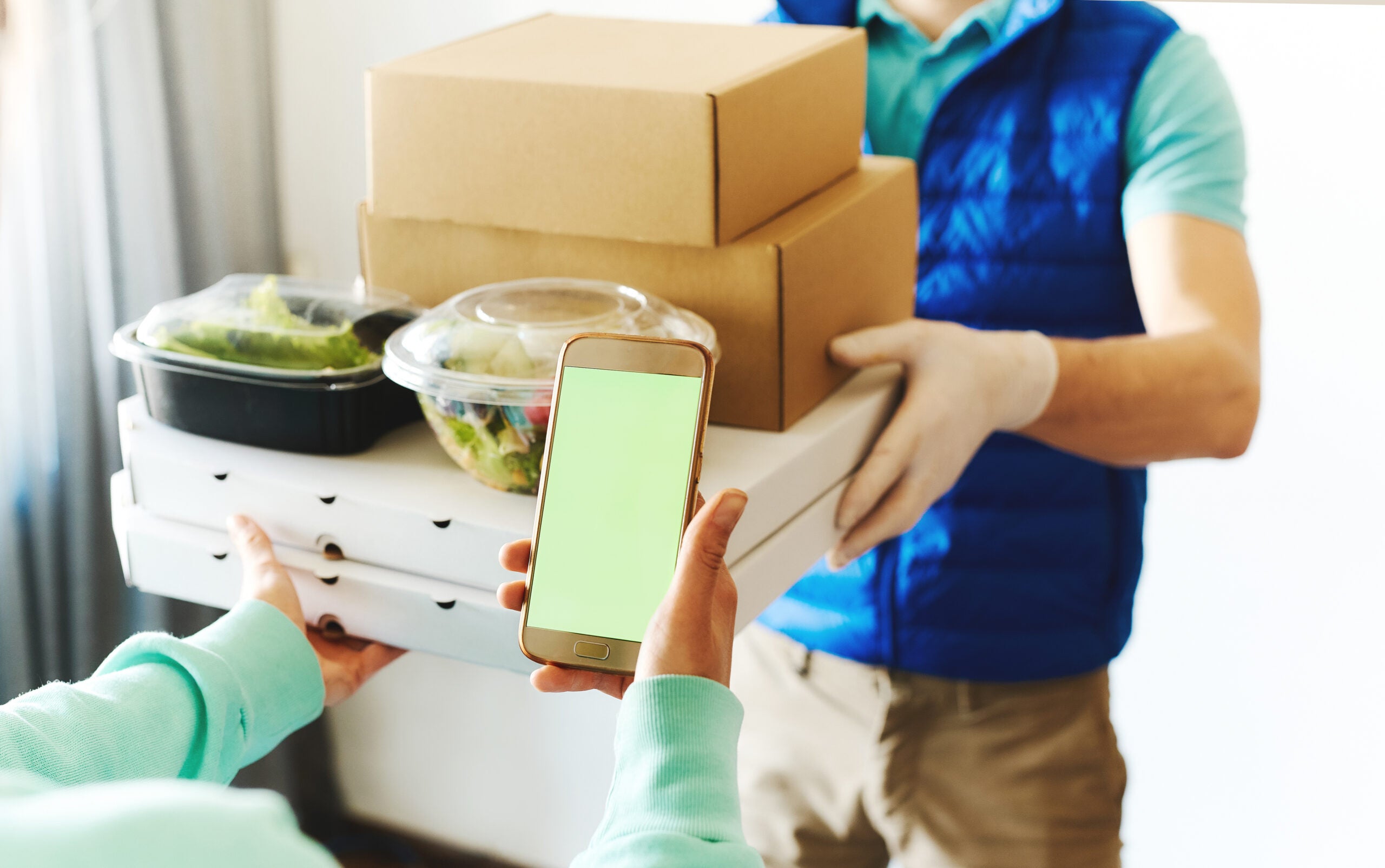 POV of woman using smarthone for ordering online, receiving takeout food from delivery man.